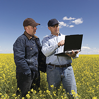 Photo of two people looking at a laptop while standing in a field