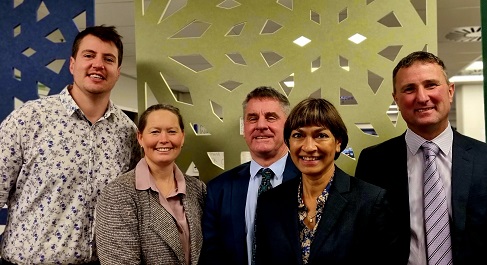 Photograph of five people standing in front of a yellow wall. 