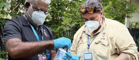2 masked indigenous rangers viewing and discussing a specimen tube.