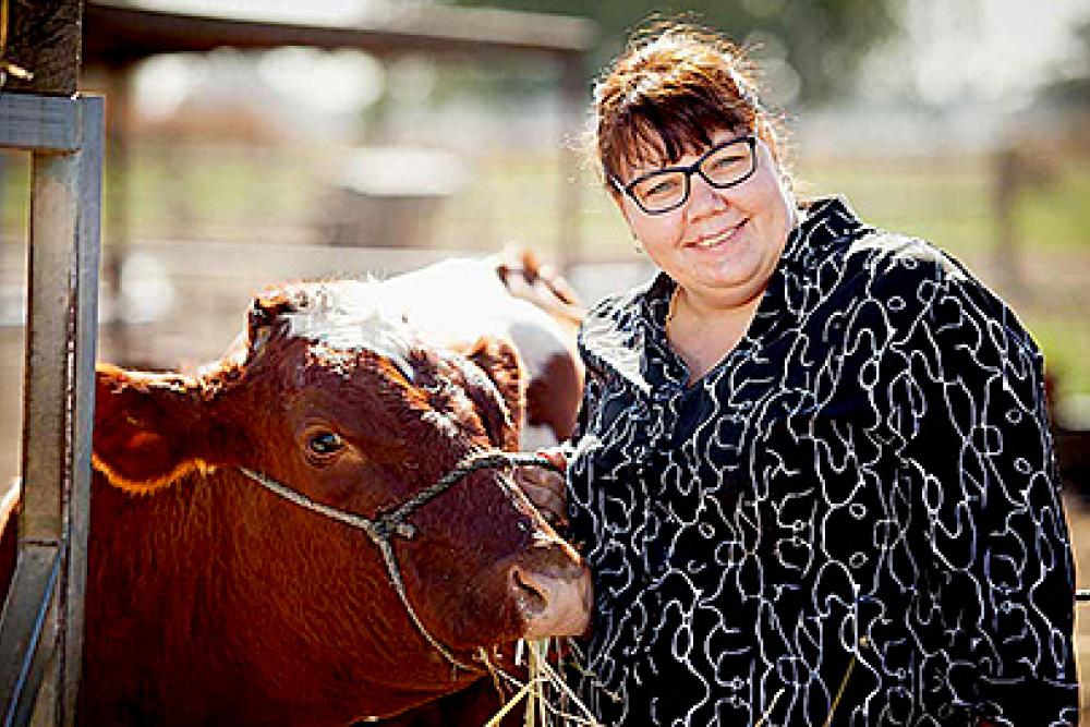 Image of a smiling person next to a cow that is eating some hay