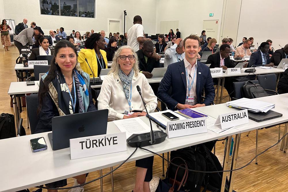 Three people sitting at a table in a room full of people