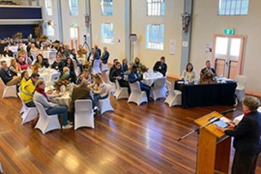 Image of a hall with people sitting at tables and a lectern at the front 