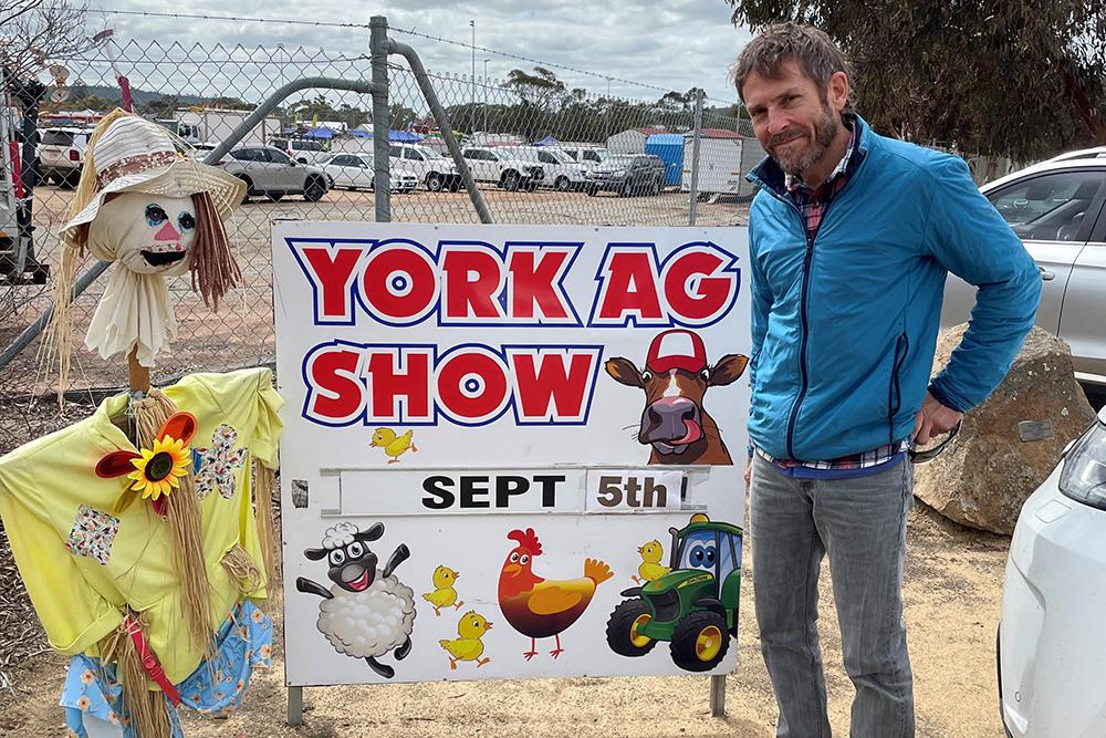 A person standing next to a scarecrow and a sign saying "York Ag Show, Sept 6th"