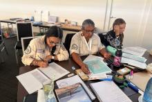 3 First Nations biosecurity students studying at a large desk surrounded by books in a classroom