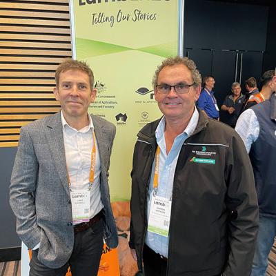 Chris Rodwell and Darren Spencer stand in front of a Lambex26 poster and several people at the event.